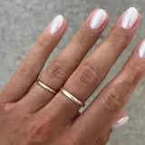 Dłoń z perłowym francuskim manicure i złotymi obrączkami.