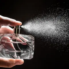 Dłoń trzyma szklaną butelkę, z której rozpyla się mgiełka. Czy to woda toaletowa czy perfumowana?