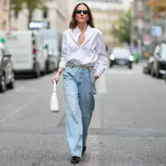 Kobieta w luźnych, jasnych jeansach typu mom fit i białej koszuli, z białą torebką. Stylizacja dla każdej kobiety ceniącej wygodę i modny look.