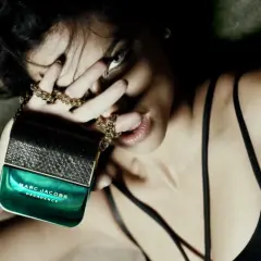 Kobieta zmysłowo trzyma flakon perfum Marc Jacobs Decadence, otoczona złotym łańcuszkiem.