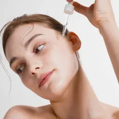 Kobieta aplikuje kroplę serum na skroń. To esencja piękna, która odżywia skórę.