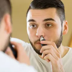Mężczyzna przycina włosy w nosie, patrząc w lustro. Dba o swój wygląd, usuwając niechciane włoski.