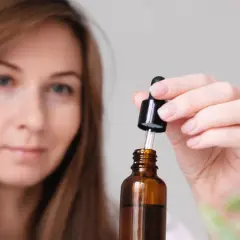 Kobieta z brązowymi włosami przygotowuje serum z disodium edta. Kroplomierz pobiera płyn z buteleczki.