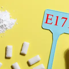 Biały proszek, tabletki i gumy do żucia na żółtym tle. Niebieska tabliczka z napisem E171.