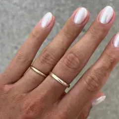 Dłoń z perłowym francuskim manicure i złotymi obrączkami.