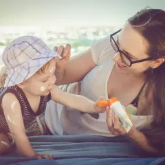 Mama smaruje dziecko kremem z filtrem na plaży. Kolastyna chroni delikatną skórę malucha przed słońcem.