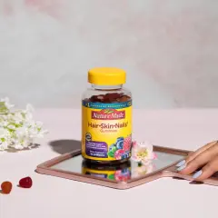 Hello gummies zdrowe włosy i paznokcie opinie. Butelka Nature Made na lustrzanej tacy, obok kwiatów i kilku żelków.