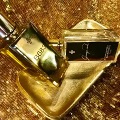 Dwa flakony perfum Marc Antoine Barrois, jeden z napisem B683, drugi z Ganymede, na złotej, cekinowej tkaninie.