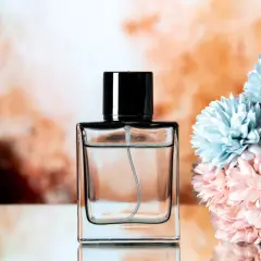 Elegancka butelka perfum z czarną nakrętką, obok bukietu błękitnych i różowych kwiatów. Klik i pachniesz opinie.