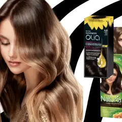 Kobieta z lśniącymi, falowanymi włosami w odcieniu czekoladowy brąz. Obok opakowania farb do włosów Garnier Olia, Joanna Naturia i Wella.