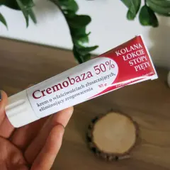 Dłoń trzyma tubkę kremu Cremobaza 50%, który pomaga na zrogowacenia. Brak informacji o skutkach ubocznych.