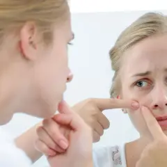 Dziewczyna z pryszczem na twarzy ogląda go w lustrze, dotykając palcem.