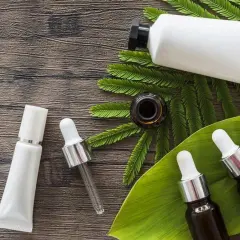 Buteleczki z serum i kremem na drewnianym tle, wśród liści. Dylemat: retinol czy retinal?