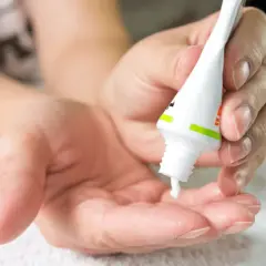 Dłoń aplikuje białą maść z tubki na drugą dłoń.