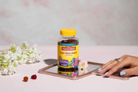 Hello gummies zdrowe włosy i paznokcie opinie. Butelka Nature Made na lustrzanej tacy, obok kwiatów i kilku żelków.