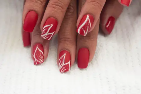 Czerwone paznokcie ze złotym zdobieniem w kształcie liści. Matowe, eleganckie, przyciągające wzrok.