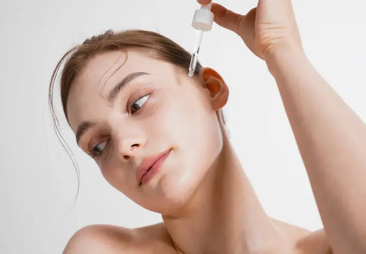 Kobieta aplikuje kroplę serum na skroń. To esencja piękna, która odżywia skórę.