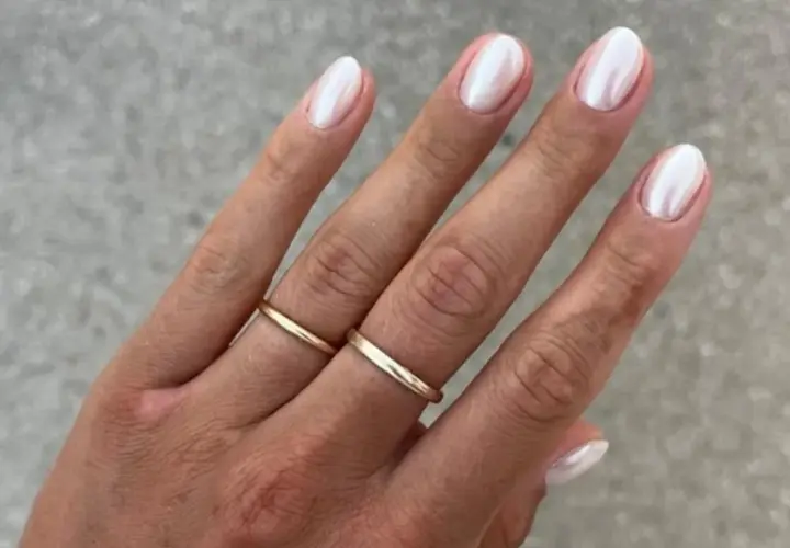 Dłoń z perłowym francuskim manicure i złotymi obrączkami.