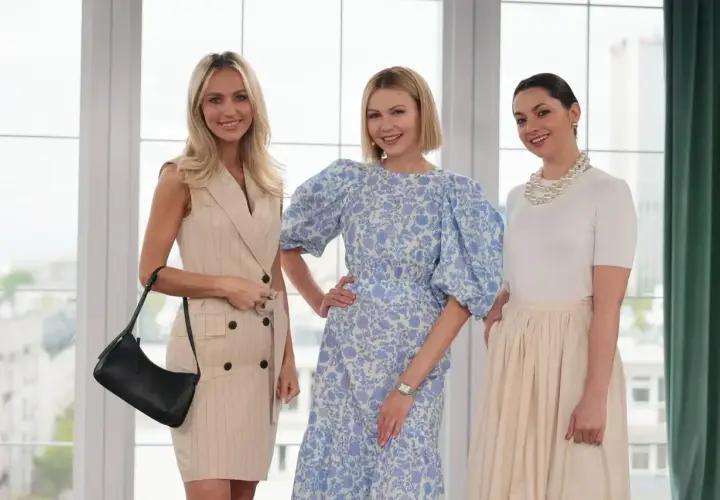Trzy kobiety prezentują eleganckie mama na komunii stylizacje. Jedna w beżowej sukience w prążki, druga w kwiecistej sukience z bufiastymi rękawami, trzecia w białej bluzce i beżowej spódnicy.