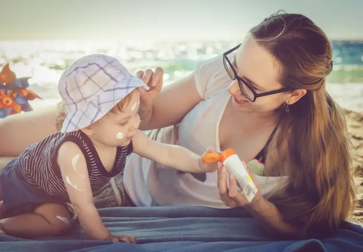 Mama smaruje dziecko kremem z filtrem na plaży. Kolastyna chroni delikatną skórę malucha przed słońcem.