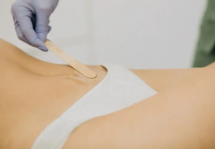 Dłoń w rękawiczce nakłada wosk szpatułką na skórę w okolicach bikini.