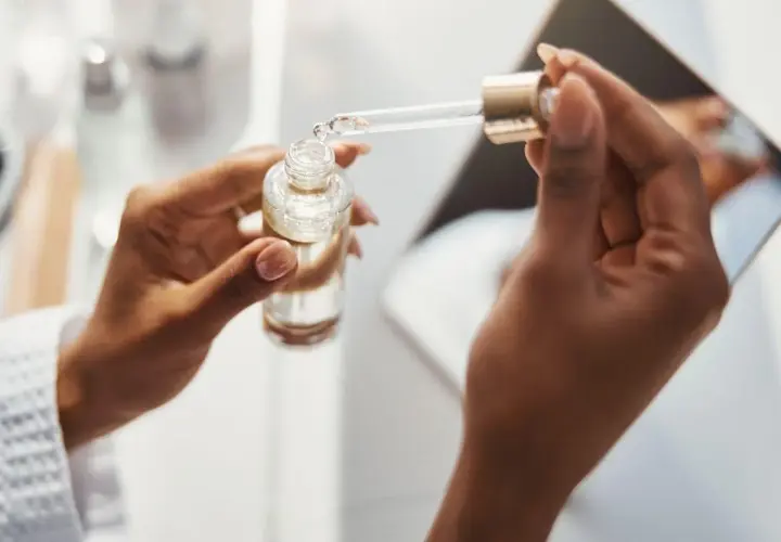 Dłonie trzymają buteleczkę z serum. Pipeta z kroplą produktu, być może zawierającego kwas ferulowy, jest gotowa do aplikacji.