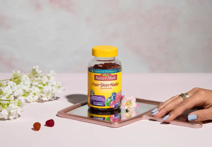 Hello gummies zdrowe włosy i paznokcie opinie. Butelka Nature Made na lustrzanej tacy, obok kwiatów i kilku żelków.