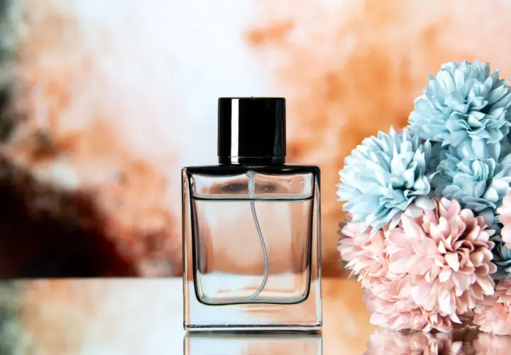 Elegancka butelka perfum z czarną nakrętką, obok bukietu błękitnych i różowych kwiatów. Klik i pachniesz opinie.