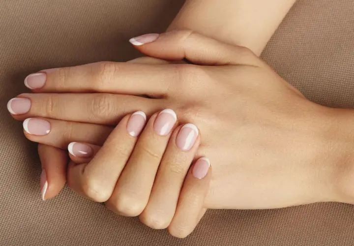 Dłonie z klasycznym francuskim manicure. Delikatny róż i biel na paznokciach, idealne dopełnienie naturalnego piękna. To kwintesencja manicure biologicznego.