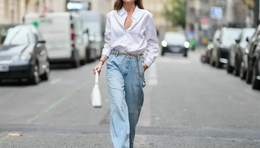 Kobieta w luźnych, jasnych jeansach typu mom fit i białej koszuli, z białą torebką. Stylizacja dla każdej kobiety ceniącej wygodę i modny look.
