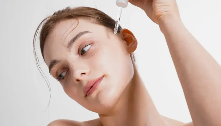 Kobieta aplikuje kroplę serum na skroń. To esencja piękna, która odżywia skórę.