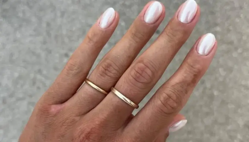 Dłoń z perłowym francuskim manicure i złotymi obrączkami.