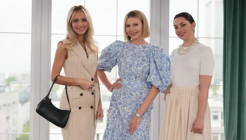 Trzy kobiety prezentują eleganckie mama na komunii stylizacje. Jedna w beżowej sukience w prążki, druga w kwiecistej sukience z bufiastymi rękawami, trzecia w białej bluzce i beżowej spódnicy.