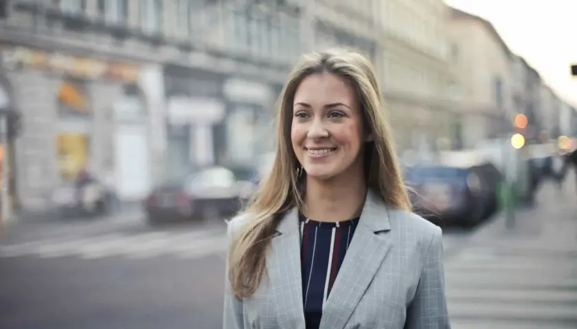Uśmiechnięta kobieta w marynarce na tle miasta. Czytała pozytywne renee opinie forum i postanowiła wybrać się na spacer.