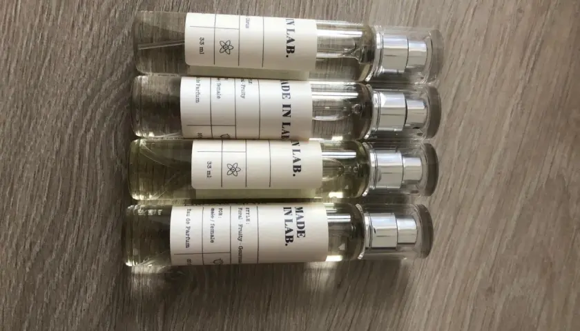 Cztery małe flakoniki perfum "MADE IN LAB." na drewnianym tle. Opinie o nich są pozytywne, doceniane za zapachy.