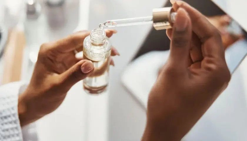 Dłonie trzymają buteleczkę z serum. Pipeta z kroplą produktu, być może zawierającego kwas ferulowy, jest gotowa do aplikacji.