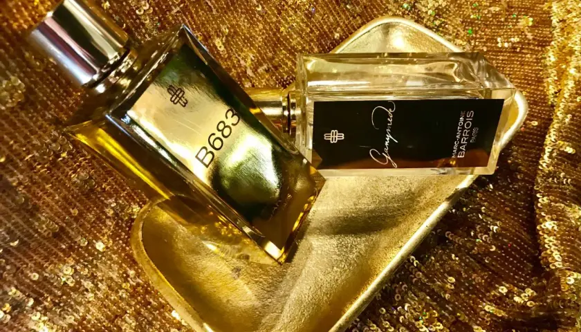 Dwa flakony perfum Marc Antoine Barrois, jeden z napisem B683, drugi z Ganymede, na złotej, cekinowej tkaninie.