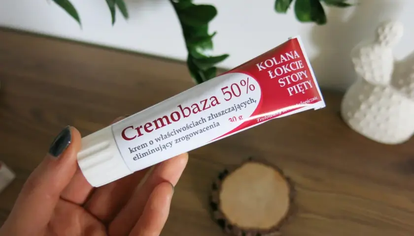Dłoń trzyma tubkę kremu Cremobaza 50%, który pomaga na zrogowacenia. Brak informacji o skutkach ubocznych.