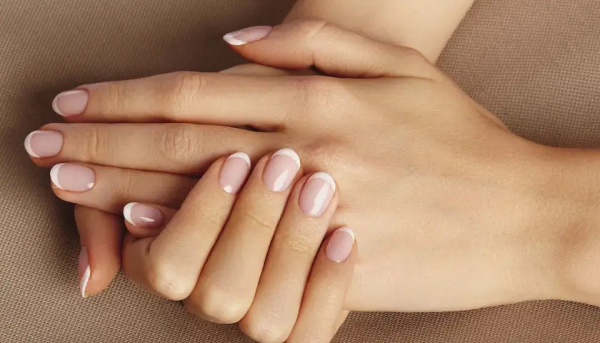 Dłonie z klasycznym francuskim manicure. Delikatny róż i biel na paznokciach, idealne dopełnienie naturalnego piękna. To kwintesencja manicure biologicznego.