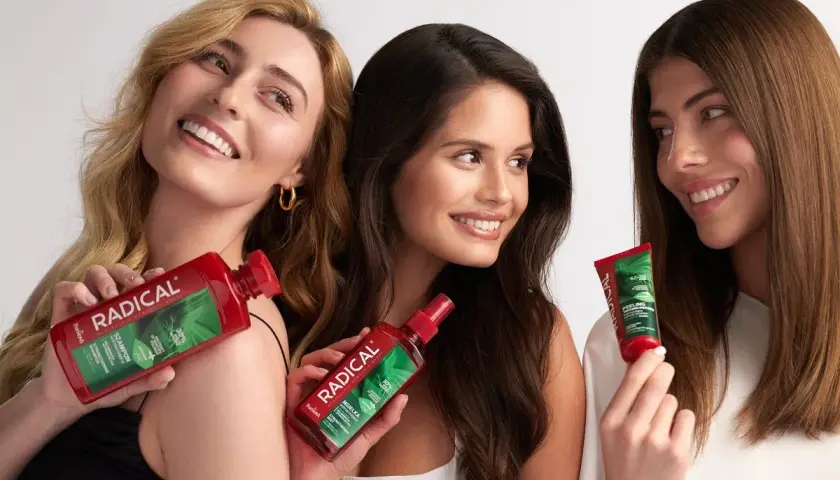Trzy uśmiechnięte kobiety prezentują produkty Radical: szampon, mgiełkę i peeling. Ich włosy lśnią, a kosmetyki obiecują radykalną pielęgnację.