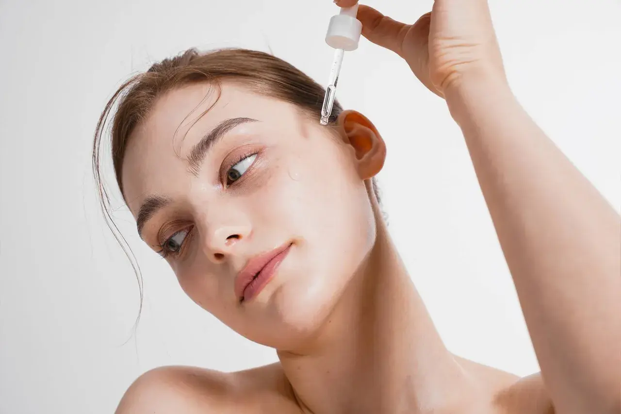 Kobieta aplikuje kroplę serum na skroń. To esencja piękna, która odżywia skórę.