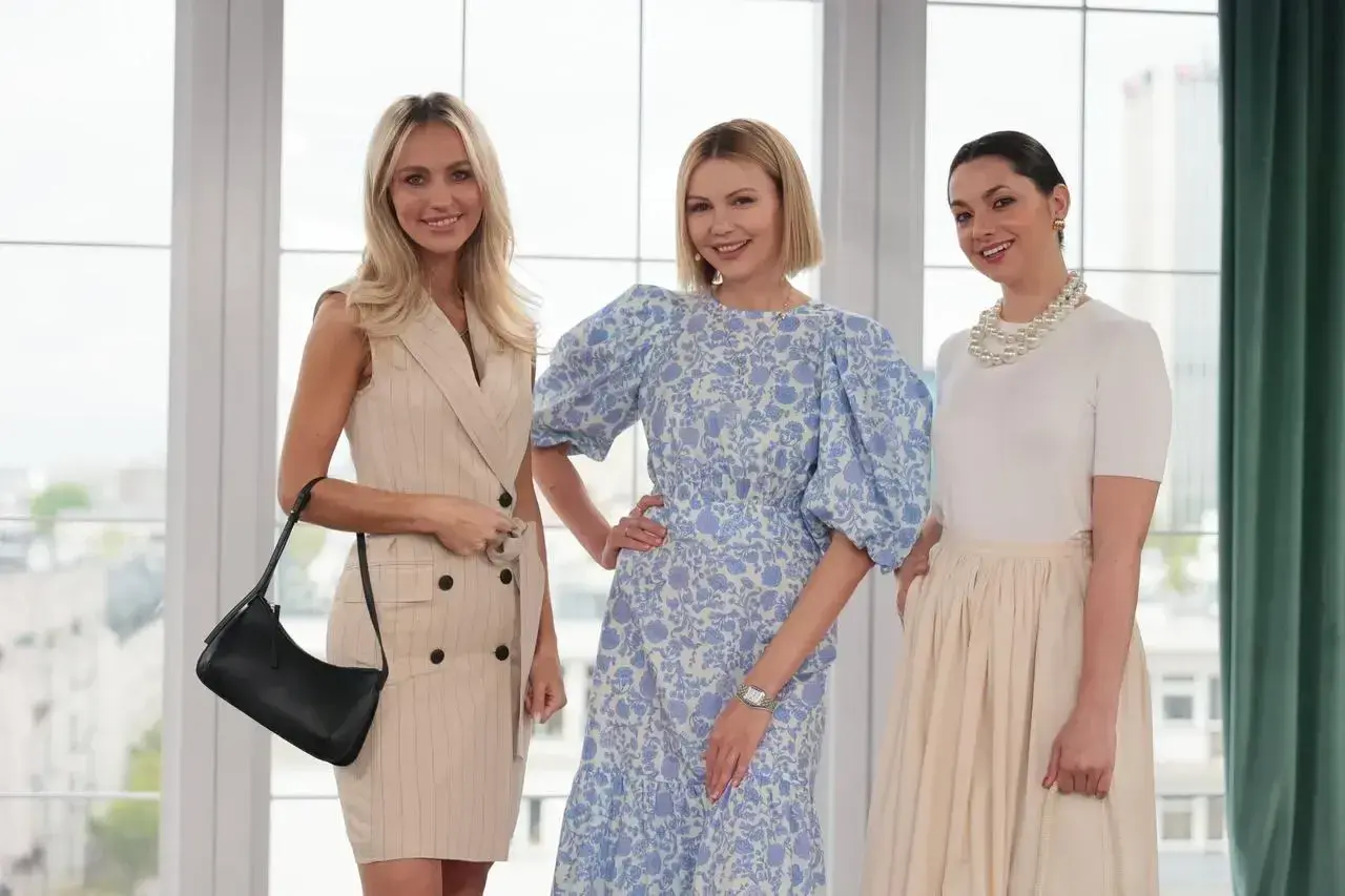 Trzy kobiety prezentują eleganckie mama na komunii stylizacje. Jedna w beżowej sukience w prążki, druga w kwiecistej sukience z bufiastymi rękawami, trzecia w białej bluzce i beżowej spódnicy.