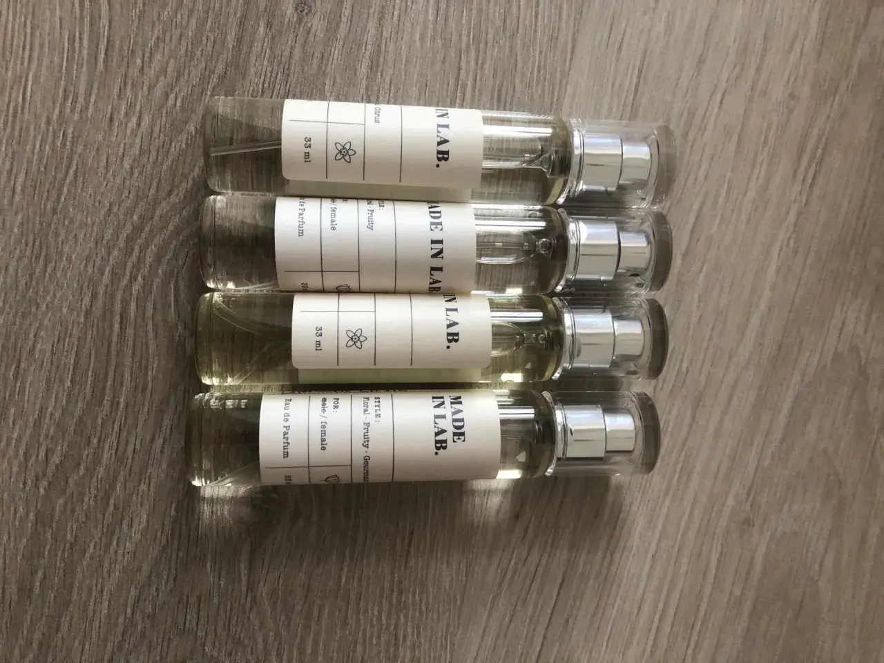 Cztery małe flakoniki perfum "MADE IN LAB." na drewnianym tle. Opinie o nich są pozytywne, doceniane za zapachy.