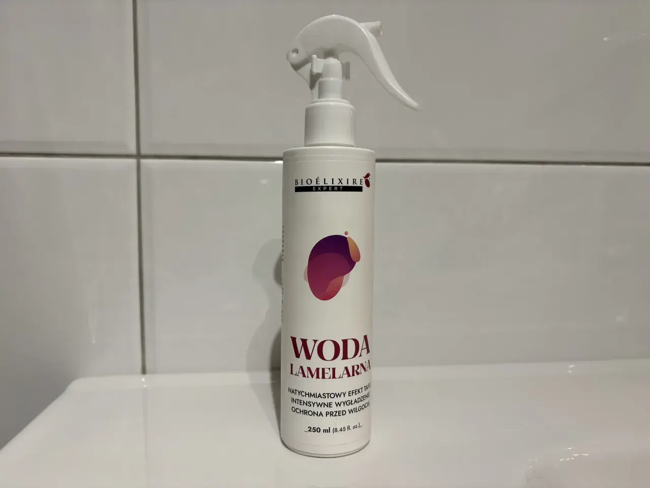 Biała butelka z atomizerem, na której widnieje napis "WODA LAMELARNA". Produkt do włosów.