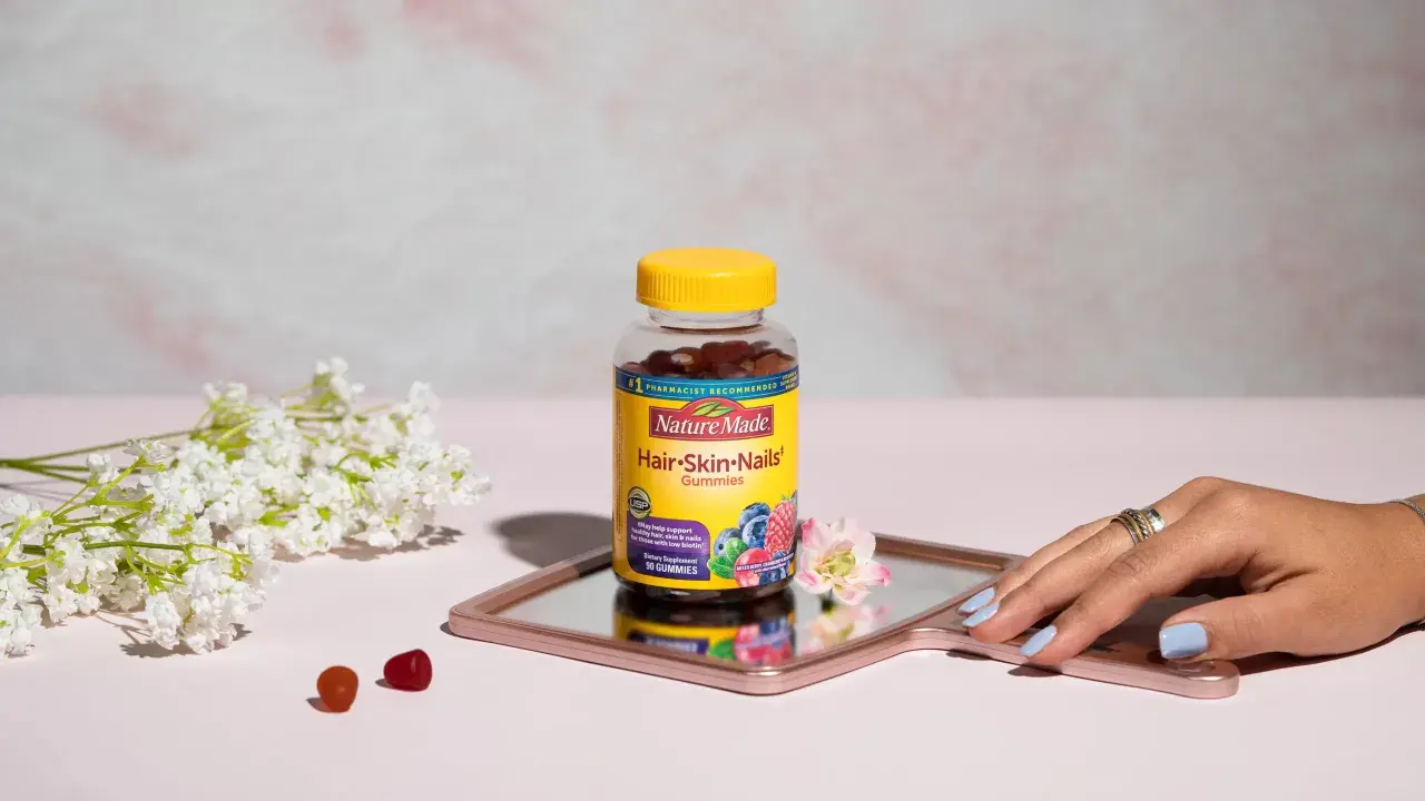 Hello gummies zdrowe włosy i paznokcie opinie. Butelka Nature Made na lustrzanej tacy, obok kwiatów i kilku żelków.