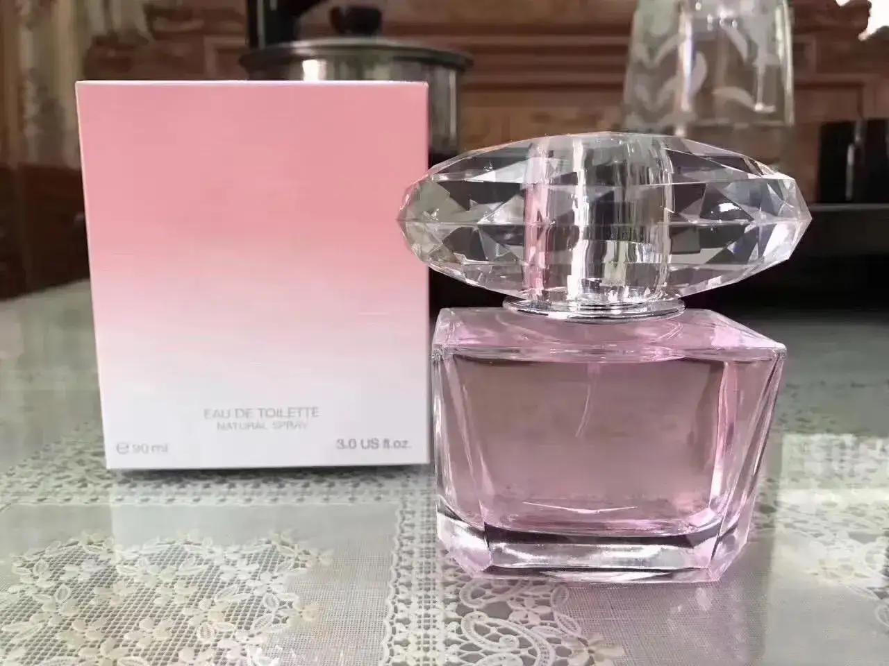 Elegancka butelka perfum lataffa yara w różowym odcieniu, z kryształowym korkiem, obok pastelowego pudełka.