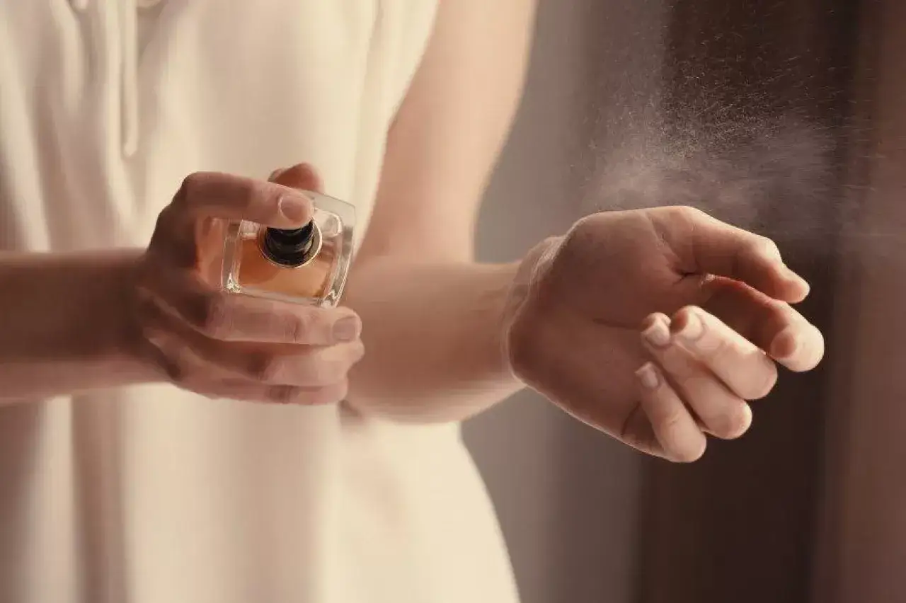 Kobieta rozpyla perfumy na nadgarstek. W powietrzu unosi się mgiełka, a w zapachu wyczuwalny jest butylfenyl metylopropional.
