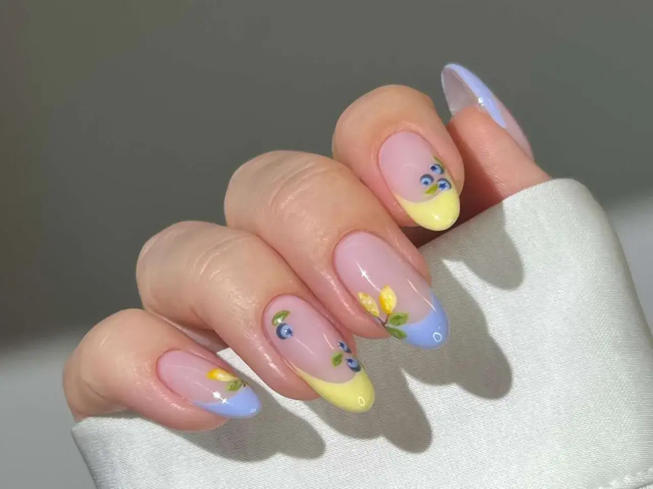 Letnia odsłona francuskiego manicure z motywem jagód i kwiatów. Paznokcie w pastelowych kolorach z delikatnymi zdobieniami.