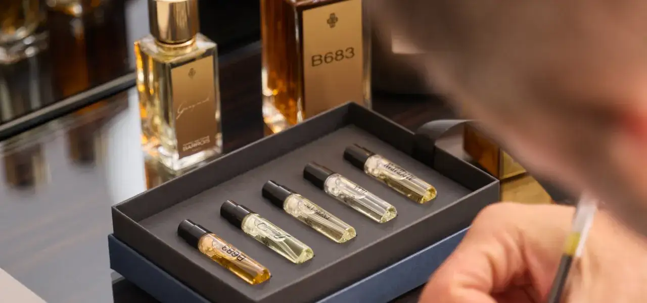 Zestaw próbek perfum od Marc Antoine Barrois w eleganckim pudełku. W tle butelki z płynami.
