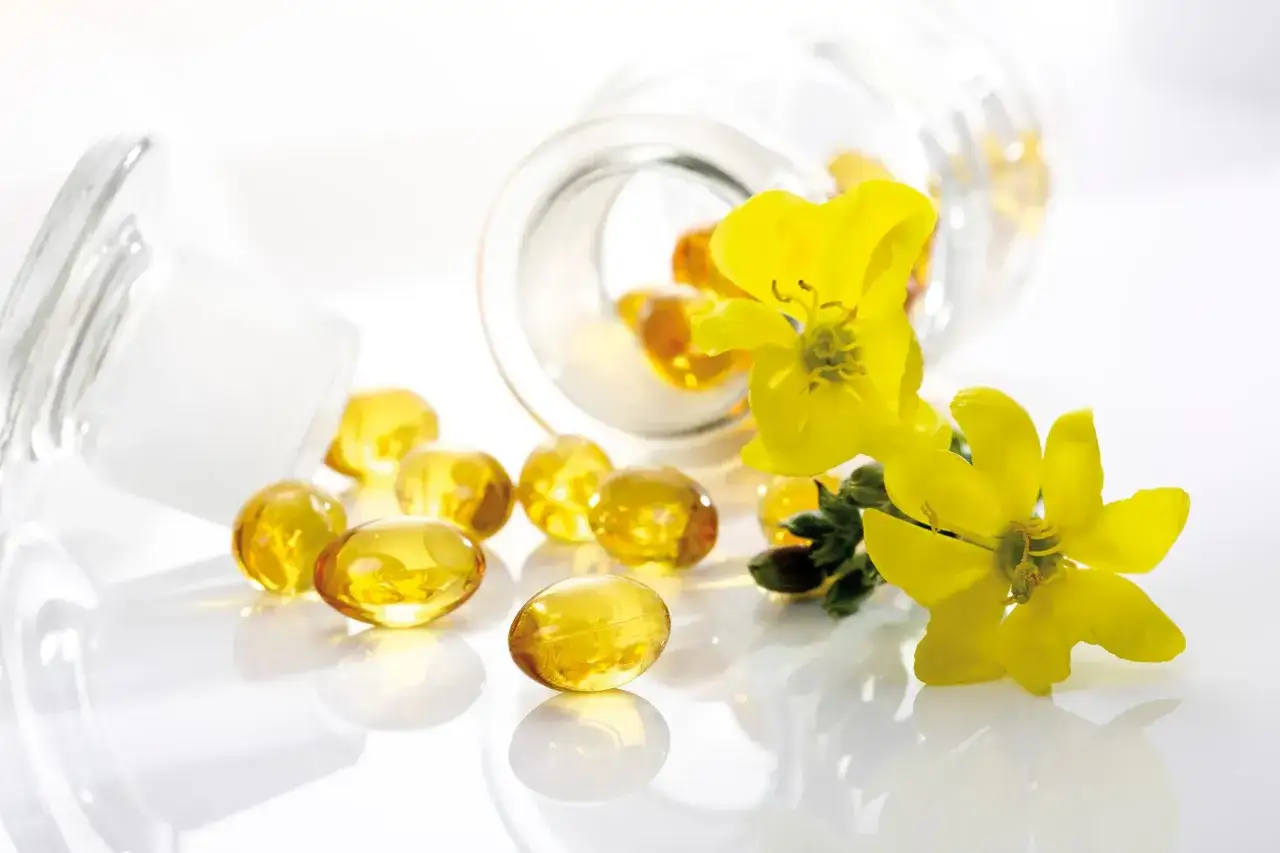 Żółte kapsułki z wiesiołka rozsypane obok otwartego słoiczka, ozdobione świeżymi kwiatami. Forum o zdrowiu.